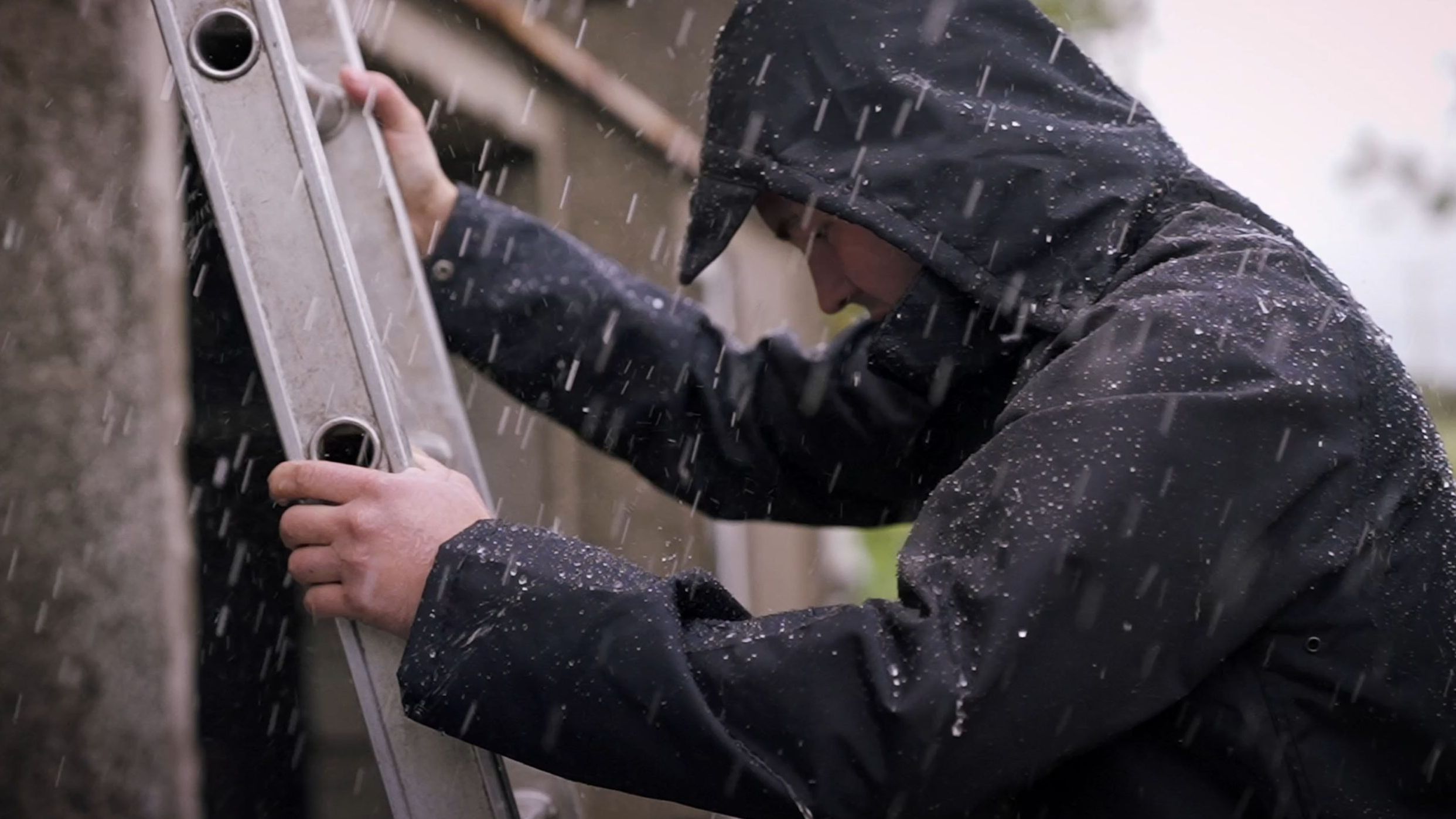 Man wearing a Cottonmount raincoat while climbing a ladder in the rain